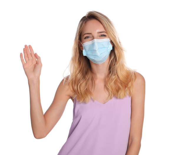 Woman in protective face mask showing hello gesture on white background. Keeping social distance during coronavirus pandemic - Photo, image