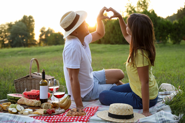 Happy couple making heart with hands on picnic in park - Foto, Bild