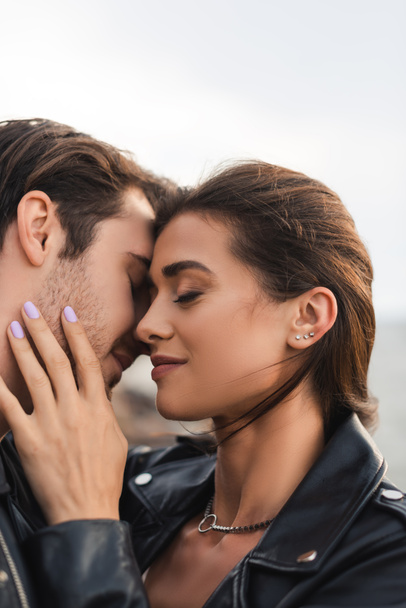 Young woman in leather jacket touching boyfriend with closed eyes outdoors  - Foto, Imagen