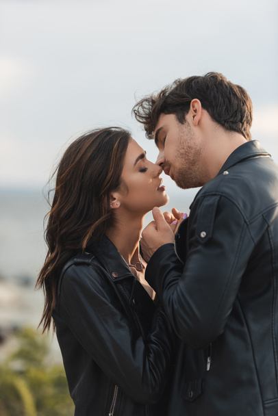 Jeune couple en vestes en cuir baisers avec les yeux fermés à l'extérieur  - Photo, image
