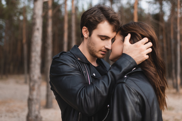 Man in leather jacket kissing and touching girlfriend in forest  - Photo, Image
