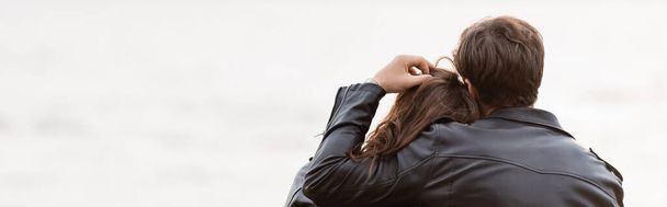 Horizontal crop of man touching hair of girlfriend in leather jacket near sea  - Foto, afbeelding