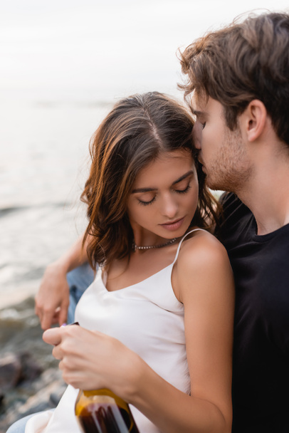 Valikoiva painopiste nuori mies suudella tyttöystävä pullo viiniä rannalla  - Valokuva, kuva