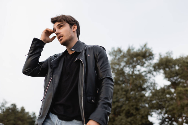 Low angle view of man in leather jacket looking away outdoors - 写真・画像