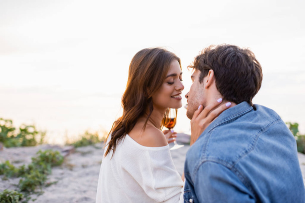 Selective focus of woman with glass of wine kissing boyfriend on beach  - Foto, afbeelding