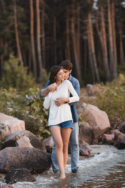 Jovem casal abraçando perto de pedras e mar na praia  - Foto, Imagem