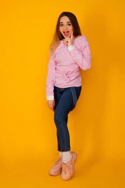 Χαρούμενη νεαρή γυναίκα σε κομψό ροζ t-shirt μείνετε σε απομονωμένη πάνω από κίτρινο φόντο - Φωτογραφία, εικόνα