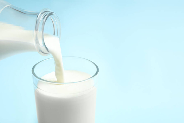 Pouring milk into glass on light blue background, closeup. Space for text - Foto, Bild