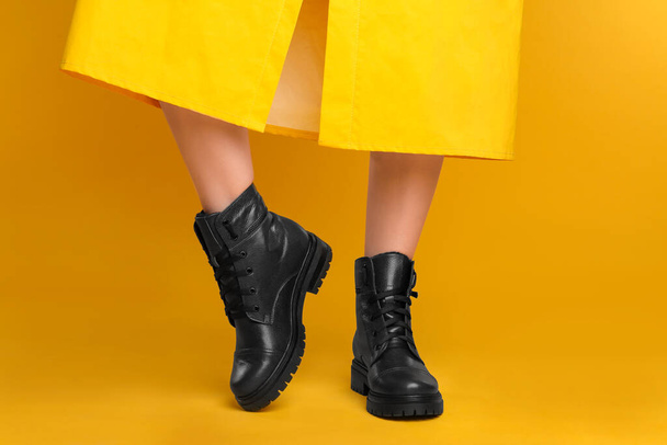 Woman wearing stylish boots on yellow background, closeup - Foto, imagen