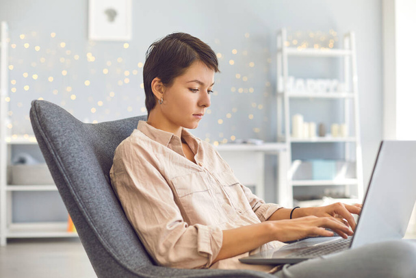 Businesswoman working on personal laptop sitting in comfortable armchair in cozy home office - Zdjęcie, obraz
