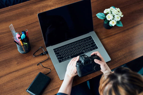 Female photographer working on photos on laptop and camera. Woman editing retouching browsing photos working as a freelancer sitting at desk - Fotografie, Obrázek