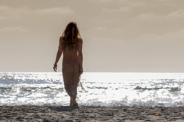 Egy gyönyörű barna bikini modell fekszik a tengerparton naplementekor. - Fotó, kép