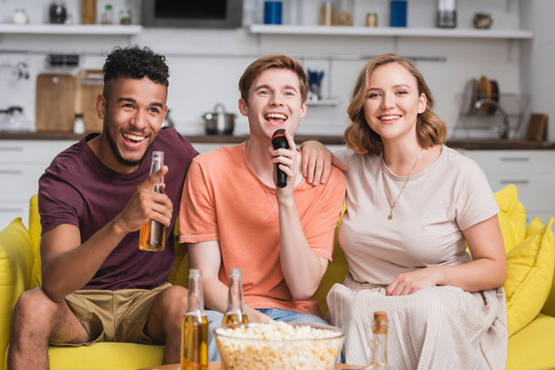 excited multicultural friends singing karaoke near beer and popcorn - Фото, зображення