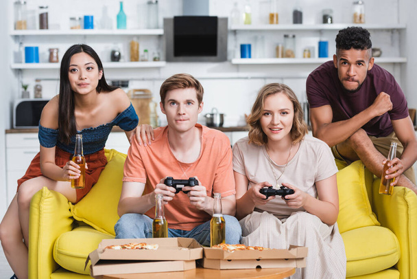 KYIV, UKRAINE - JULY 28, 2020: multicultural friends playing video game in kitchen during party - Zdjęcie, obraz