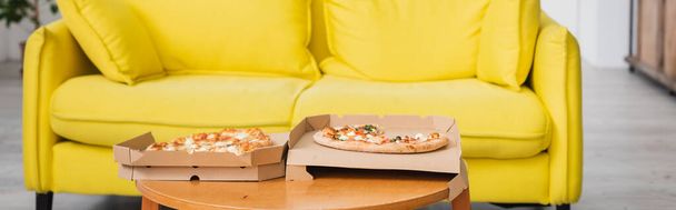 панорамный урожай вкусной пиццы на столе возле желтого дивана - Фото, изображение