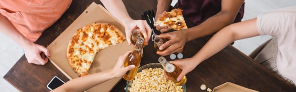 abgeschnittene Ansicht von multikulturellen Freunden, die während einer Party in der Nähe von Pizza Bierflaschen klappern, Website-Header - Foto, Bild