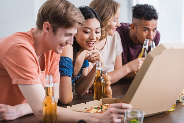 joyful multicultural friends opening box with pizza during party - Photo, Image