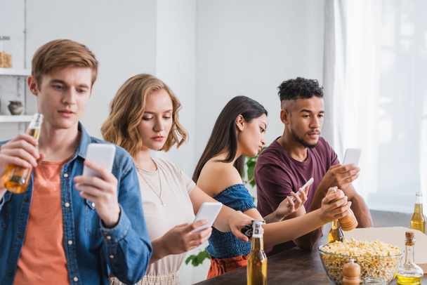 selective focus of young multicultural friends chatting on smartphones near beer and popcorn during party - Photo, image
