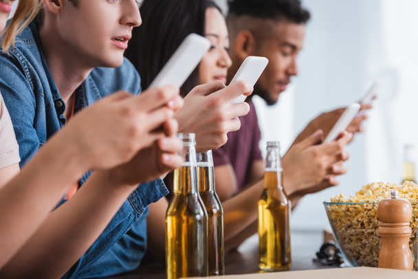 Selektiver Fokus multiethnischer Freunde, die während einer Party in der Nähe von Bier auf Smartphones chatten - Foto, Bild