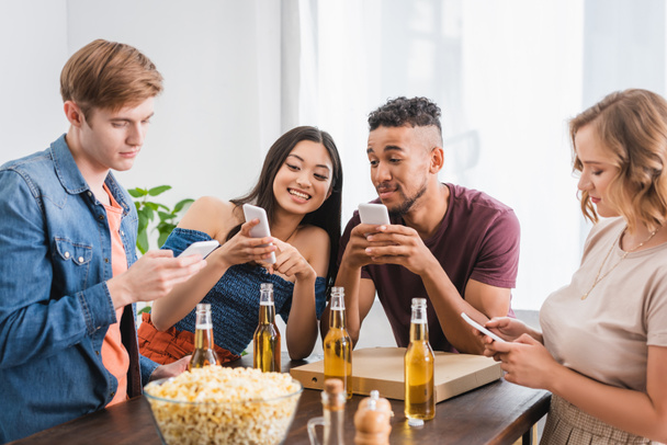 asian woman pointing with finger at smartphone near multicultural friends during party - Photo, Image