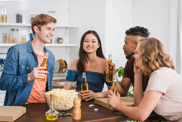 izgatott többnemzetiségű barátok kezében üveg sör és beszélgetés közben party - Fotó, kép
