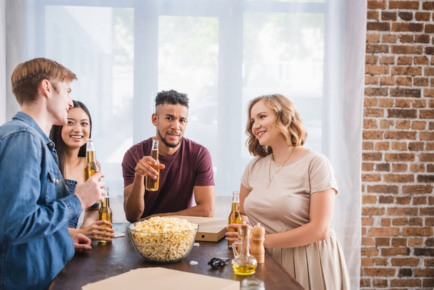 веселые мультикультурные друзья, держащие бутылки пива и разговаривающие во время вечеринки - Фото, изображение