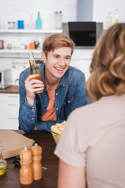 Selektiver Fokus des fröhlichen jungen Mannes, der eine Flasche Bier in der Nähe seines Freundes hält - Foto, Bild