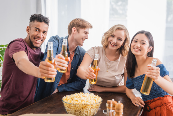 excited multicultural friends looking at camera while holding bottles of beer  - Фото, изображение