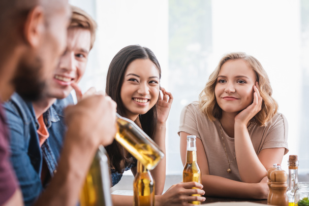 foco seletivo de amigos multiculturais alegres com garrafas de cerveja conversando durante a festa - Foto, Imagem