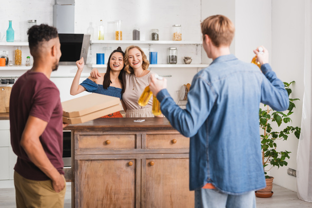 back view of multicultural friends holding pizza boxes and beer near women showing yeah gesture - Photo, Image