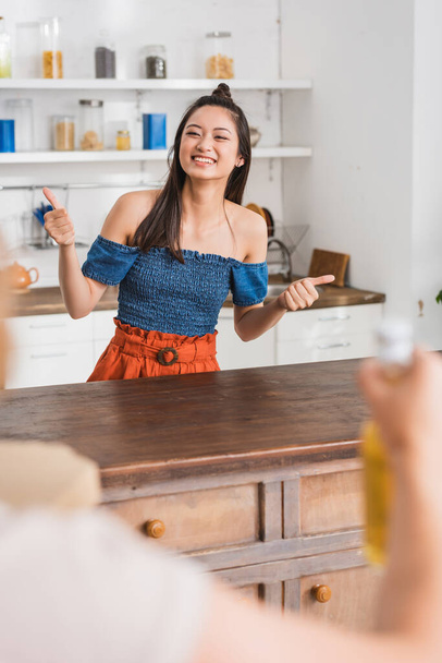 台所に親指を立てる女性と楽しいアジアの友人の選択的な焦点 - 写真・画像