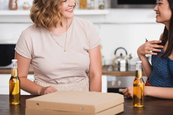 cropped view of multiethnic friends talking near beer and pizza box during party - Φωτογραφία, εικόνα