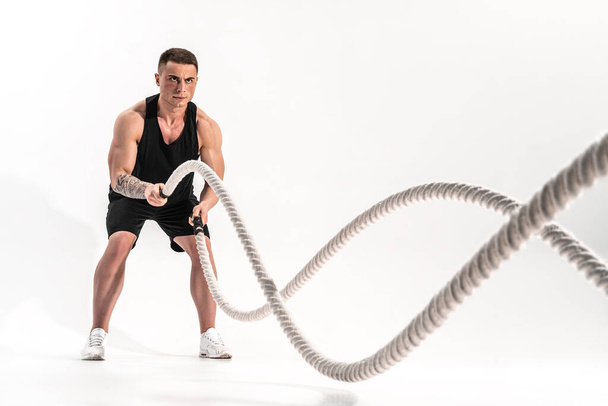 Attractive muscular man working out with heavy ropes. Photo of handsome man in sportswear isolated on white background - Foto, Bild