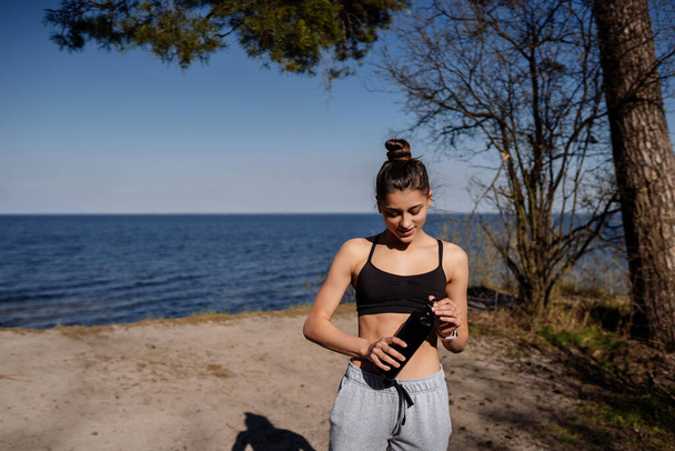 Тонкая молодая женщина пьет воду после тренировки - Фото, изображение