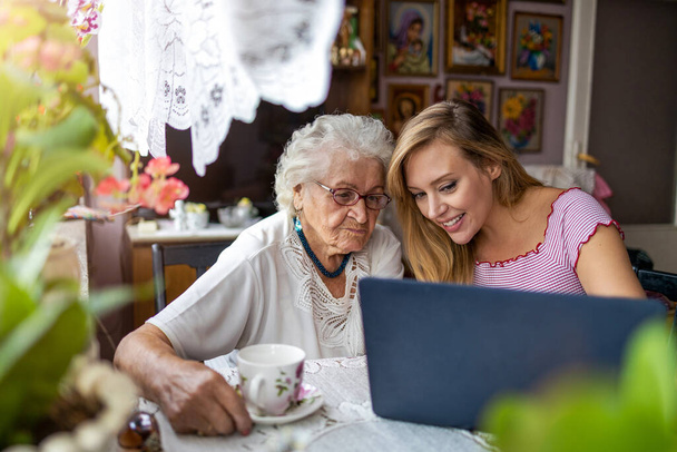 Volwassen kleindochter leert haar oudere oma laptop te gebruiken - Foto, afbeelding