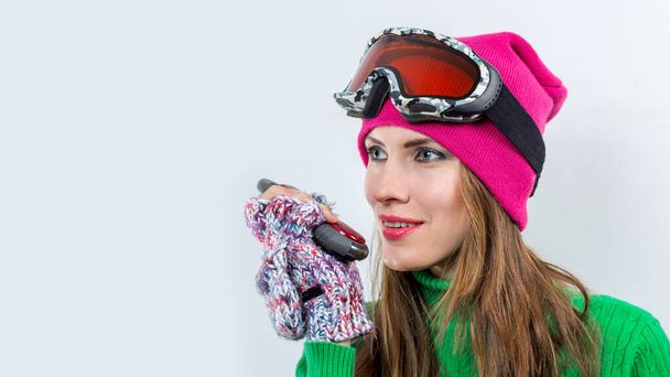 Ski woman wearing winter clothes, goggles, green sweater isolated over white holding walkie-talkie - Fotografie, Obrázek