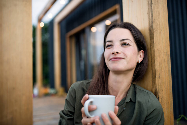 Young woman with coffee outdoors, weekend away in container house in countryside. - Foto, imagen