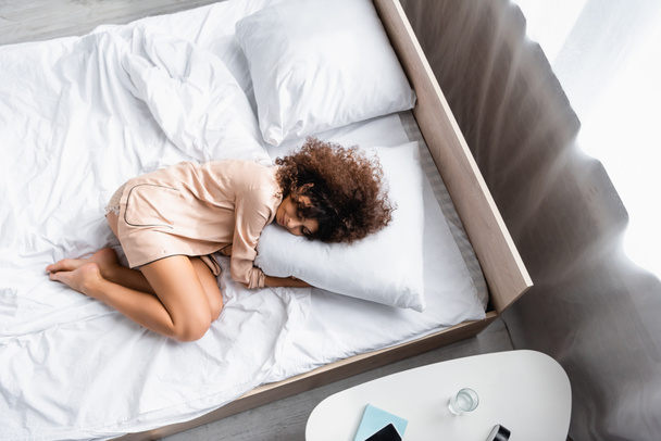 vista superior de mujer descalza con los ojos cerrados abrazando almohada mientras duerme en la cama - Foto, imagen