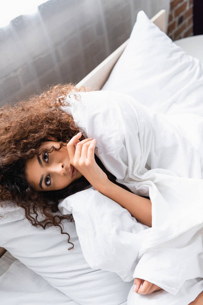 high angle view of curly woman wrapped in white blanket looking at camera  - Photo, Image