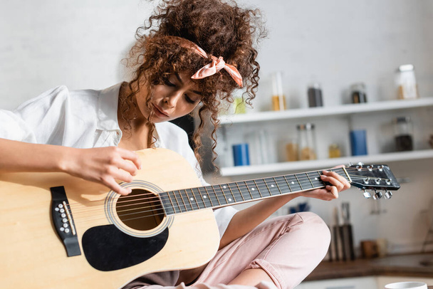 young curly woman playing acoustic guitar at home - Foto, afbeelding