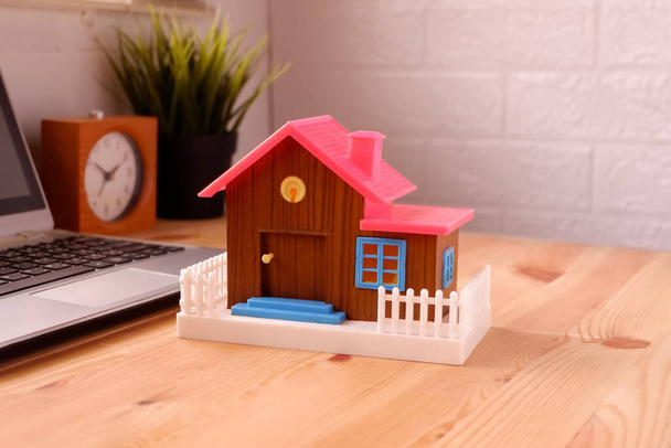 Casa de brinquedo na mesa com computador portátil, O conceito de comprar uma casa de sonho para iniciantes trabalhando - Foto, Imagem