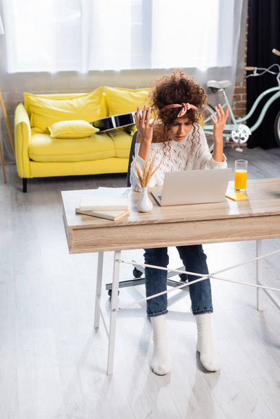 gesto freelancer descontente enquanto olha para laptop perto de livros e vidro de suco de laranja na mesa - Foto, Imagem