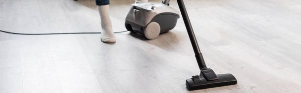 panoramic crop of woman using vacuum cleaner while cleaning home - Foto, imagen
