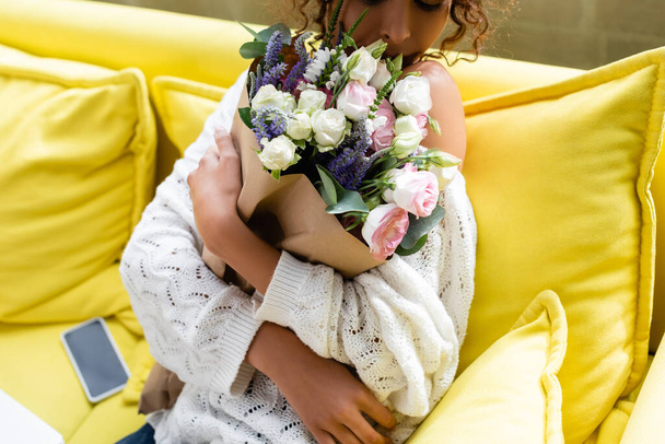 vista recortada de la joven mujer sosteniendo ramo y oliendo flores en la sala de estar - Foto, Imagen