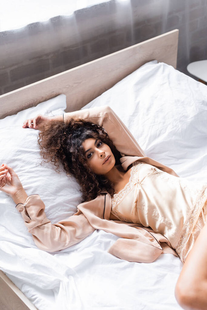 високий кут зору кучерявий і молода жінка в піжамі лежить на ліжку
 - Фото, зображення