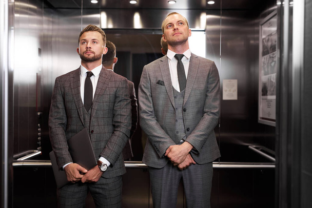 два серьезных бизнесмена встретились в лифте, ожидая, чтобы выйти оттуда - Фото, изображение