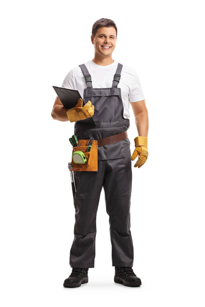 Full length portrait of a male worker with a tool belt holding a clipboard isolated on white background - Фото, изображение