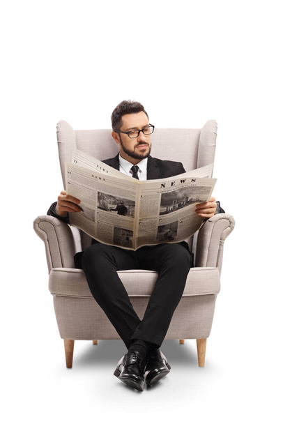 Profesional man in a black suit sitting in an armchair reading a newspaper isolated on white background - Foto, imagen