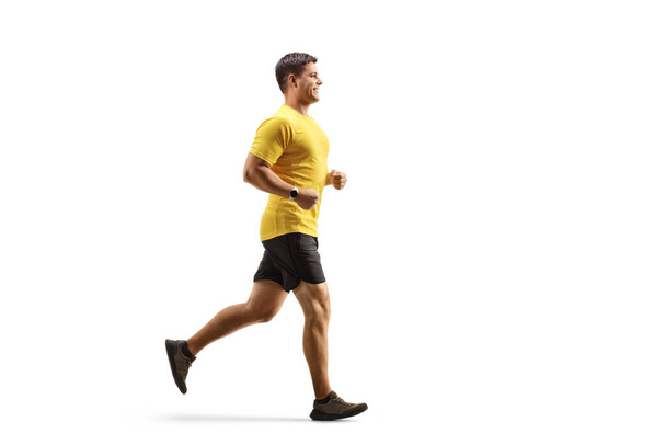 Full length profile shot of a fit man in a yellow t-shirt and black shorts running isolated on white background - Fotó, kép