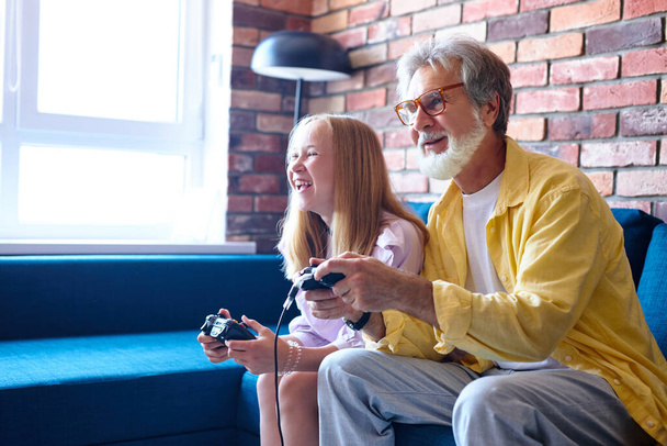 family activities. caucasian child and her grandfather playing video games - Foto, Bild